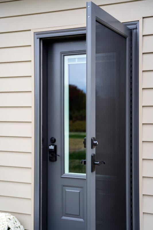 Charcoal entry door with a sleek glass insert and modern hardware, paired with a full-view aluminum storm door, offering added protection, ventilation, and a clean, contemporary look against light siding.