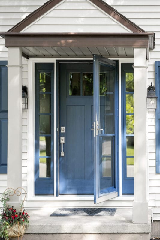 Front entry with a blue door and matching sidelights, featuring a glass storm door, white trim, and a small covered porch with columns.