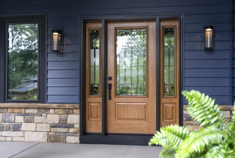 Brown entry door with blue vinyl siding. A fern sits int he foreground.