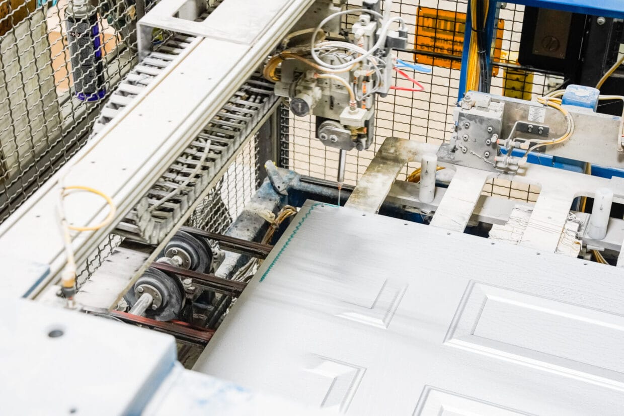 Close-up of automated machinery applying detailing to a door panel on a conveyor system inside a manufacturing facility